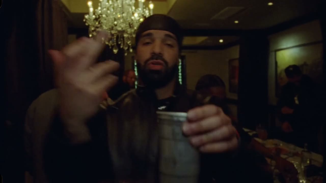 Source clip of a lead performer holding a metal cup in a crowded room with warm pendant lights