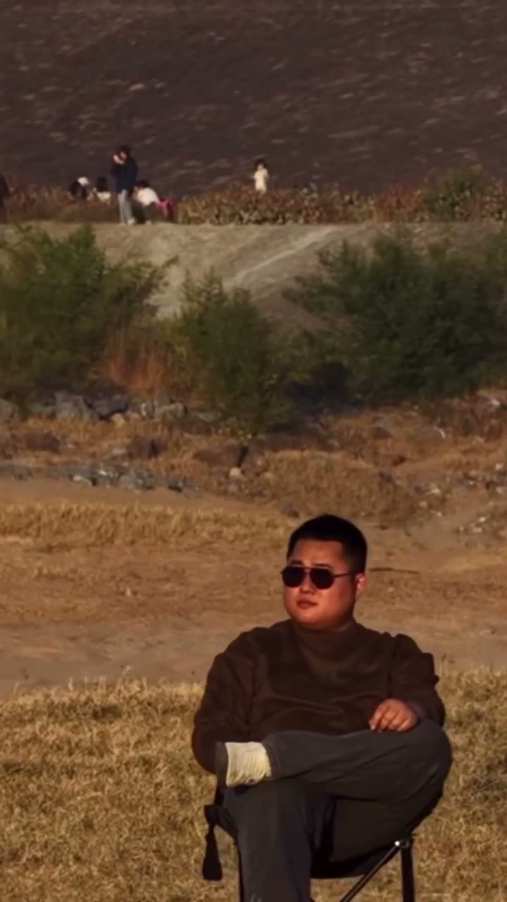 Original vertical source clip of a person seated in a folding chair while a vehicle jumps behind them